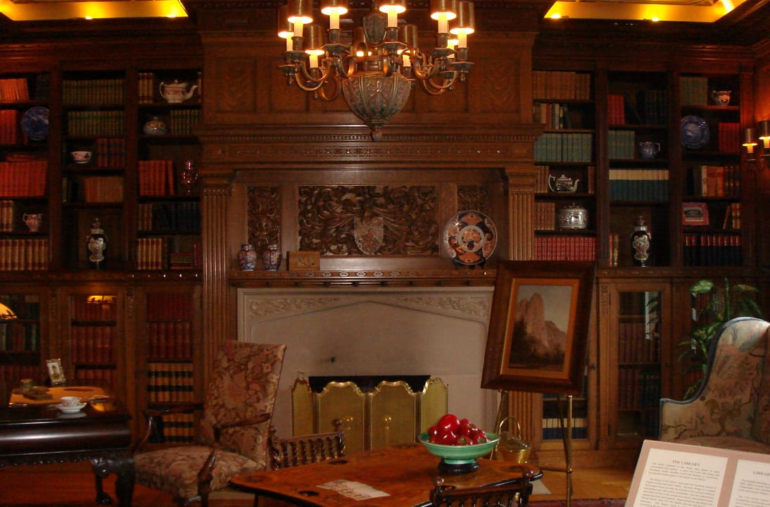 The wood-paneled library/drawing room inside the Pittock Mansion, Portland, Oregon, with its carved fireplace and built-in bookshelves.