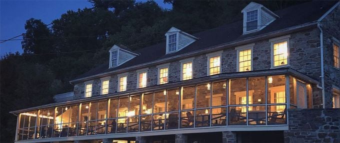 Night exterior of the historic stone Accomac Inn along the Susquehanna River in York County, Pennsylvania, with glowing windows and wooded hillside