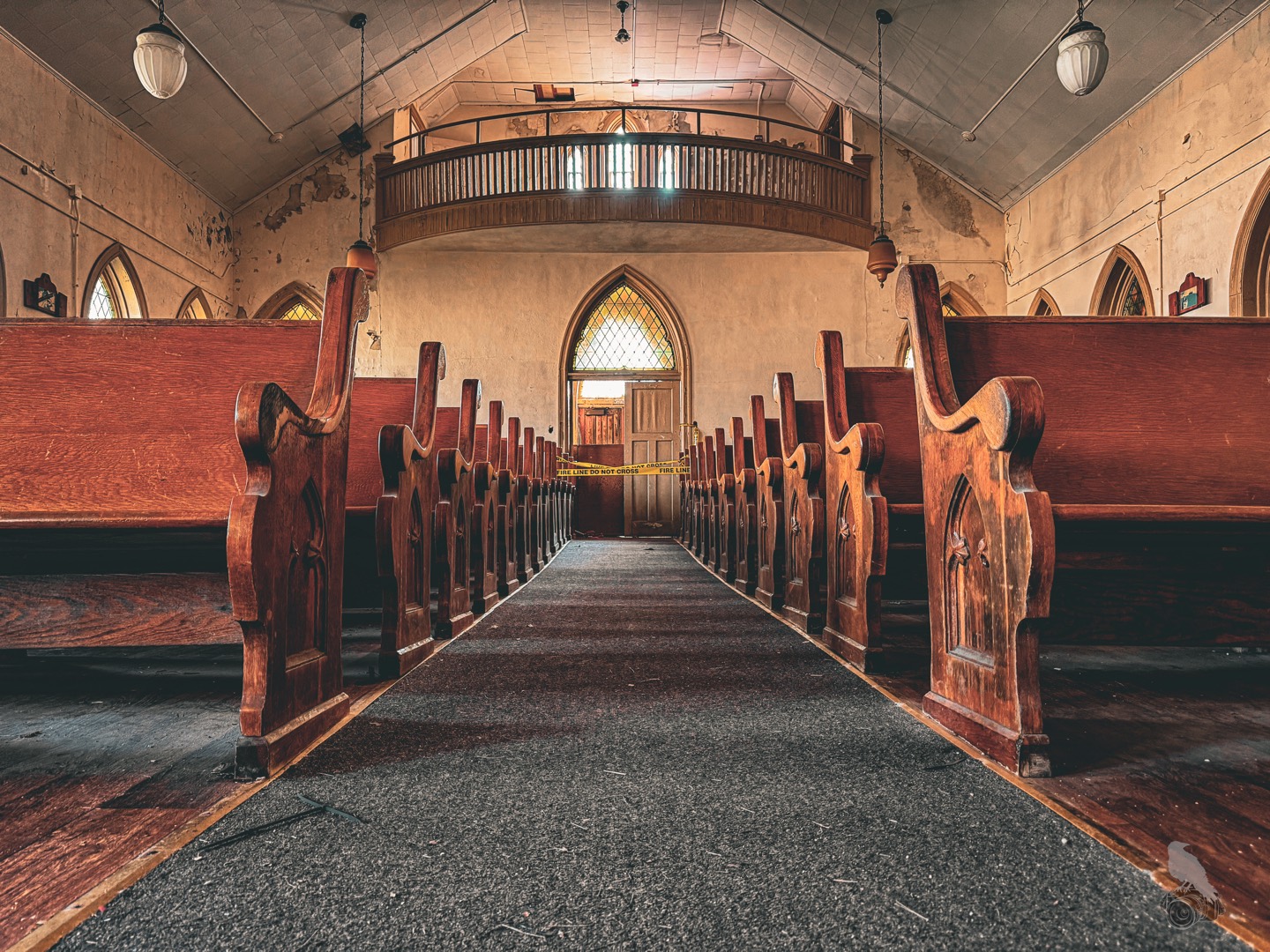 Rows of wooden pews line the carpeted aisle of Grace Chapel at Cresson Sanatorium and Prison, with a balcony and a pointed-arch window at the far end.