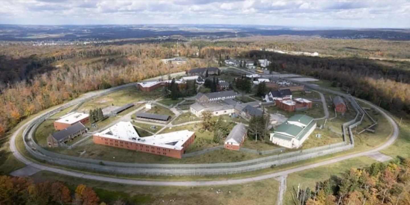 Aerial view of the Cresson Sanatorium and Prison campus: brick and stone buildings inside a ring of perimeter fence, with autumn woods beyond.