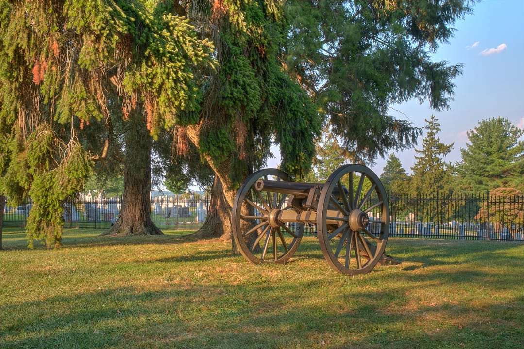 A Napoleon cannon shaded by trees at the edge of Soldiers' National Cemetery, Gettysburg National Military Park.