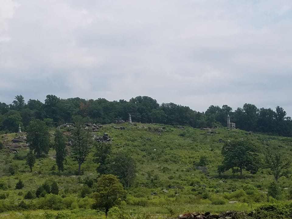 A rocky, wooded hill within Gettysburg National Military Park, with battlefield monuments visible among the boulders.