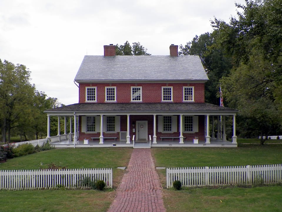 The brick front of the Edward Hand House at Rock Ford, with its picket-fenced front walk, in early-autumn foliage.