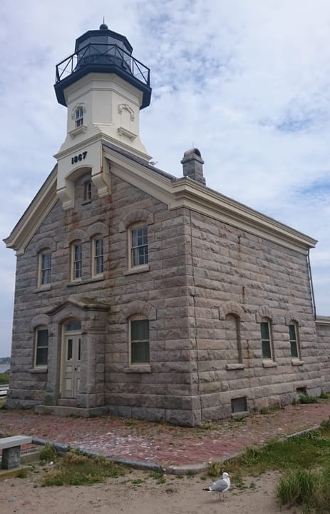 A close vertical view of Block Island North Light's tower and granite keeper's house at Sandy Point, with its 1867 datestone over the door.