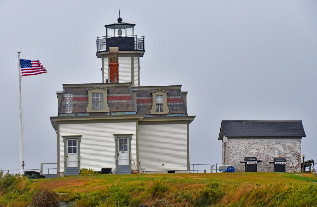 Rose Island Lighthouse viewed across the rocky bastion, with a small boat passing in the foreground.