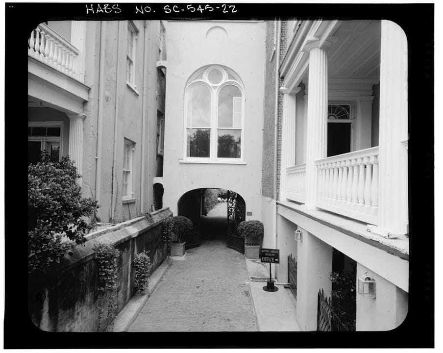 The arched carriageway and courtyard entrance of the Stevens-Lathers House (20 South Battery / Battery Carriage House Inn), Charleston, South Carolina, with its piazza columns and arched window.