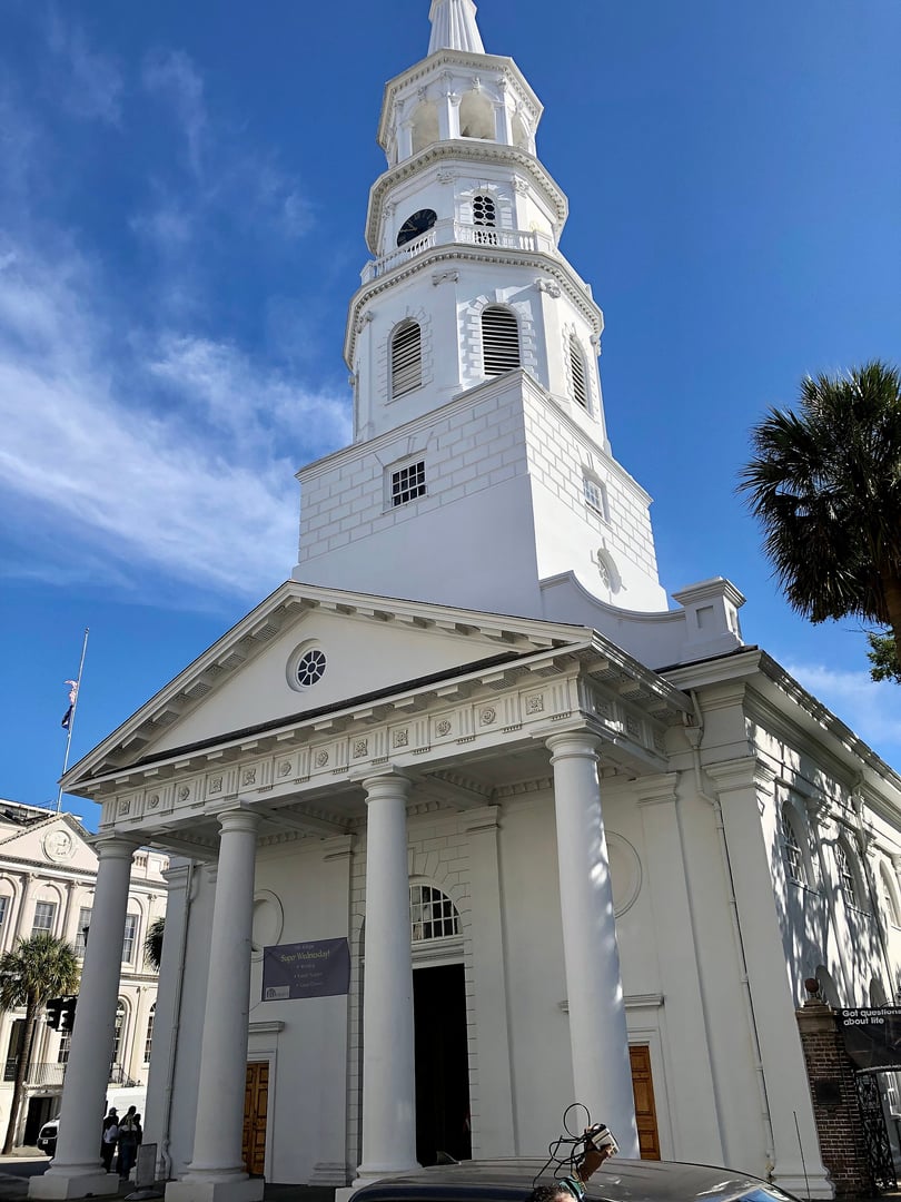 Exterior of St. Michael's Episcopal Church showing its colonial-era Tuscan portico and tall white steeple at the Four Corners of Law in Charleston's French Quarter.
