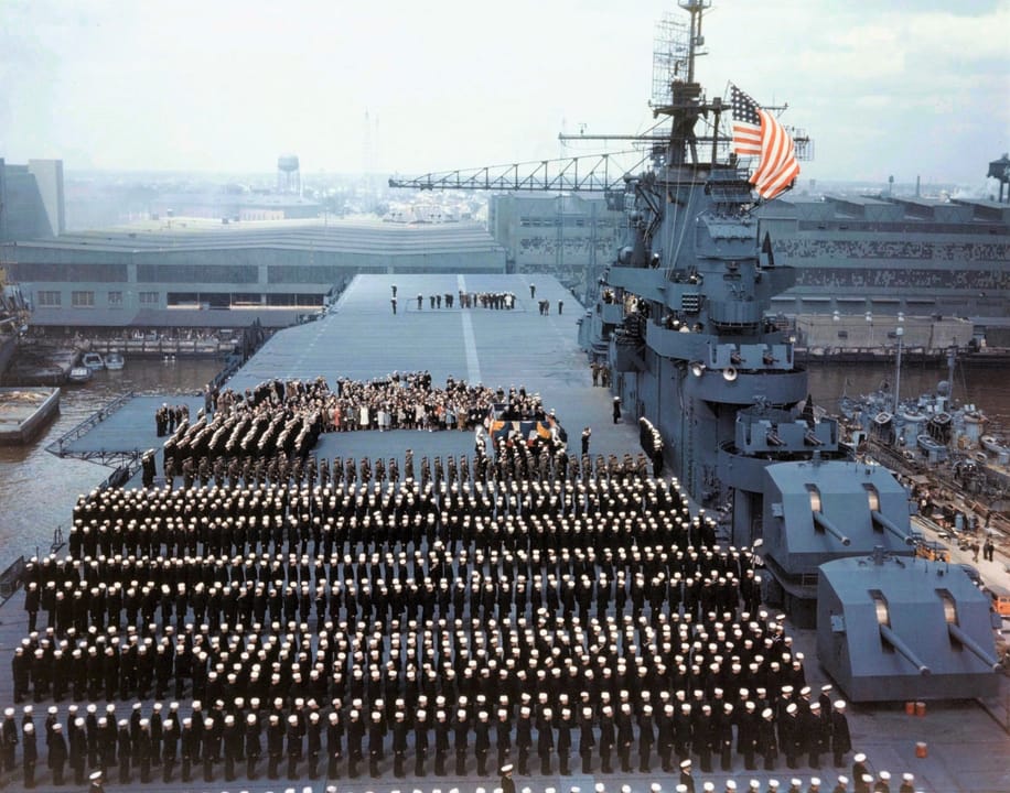The crew of USS Yorktown (CV-10) stands at attention as the national ensign is raised during commissioning ceremonies at Norfolk Navy Yard, Virginia, 15 April 1943.