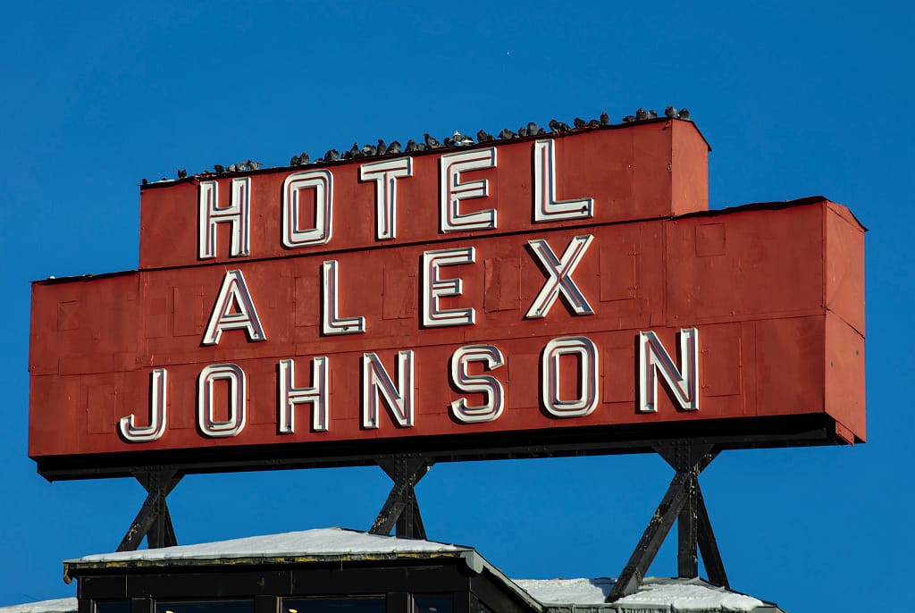The red 'HOTEL ALEX JOHNSON' rooftop neon sign against a winter sky, snow on the roofline below it. Photographed by Carol M. Highsmith, 2021, Library of Congress.