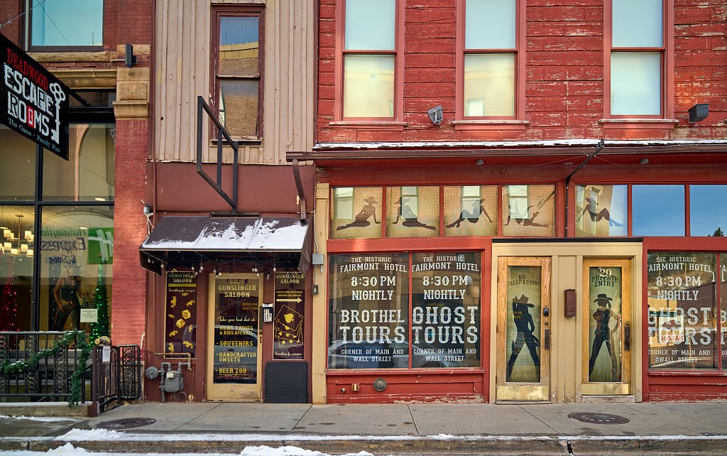 The Fairmont Hotel's red-brick Main Street storefront entrance, with its Ghost Tours and Brothel Tours signage, Deadwood, South Dakota, 2021.