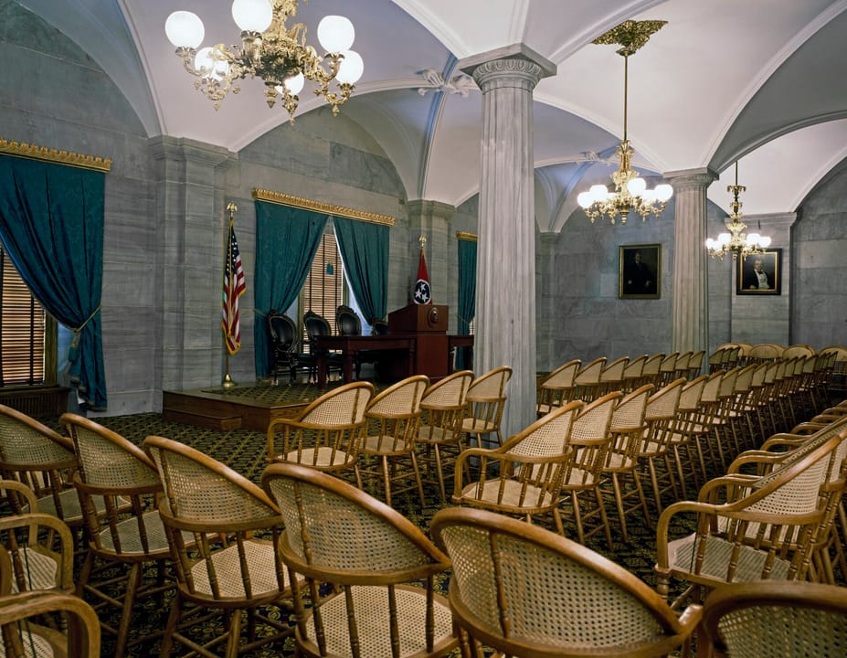 A vaulted, column-lined hearing room inside the Tennessee State Capitol, set with rows of cane-back chairs.