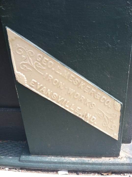 This pressed emblem appears on exterior columns around the Hancock Building with text stating, "Geo. L. Mesker &amp; Co. Iron Works, Evansville, Ind.".