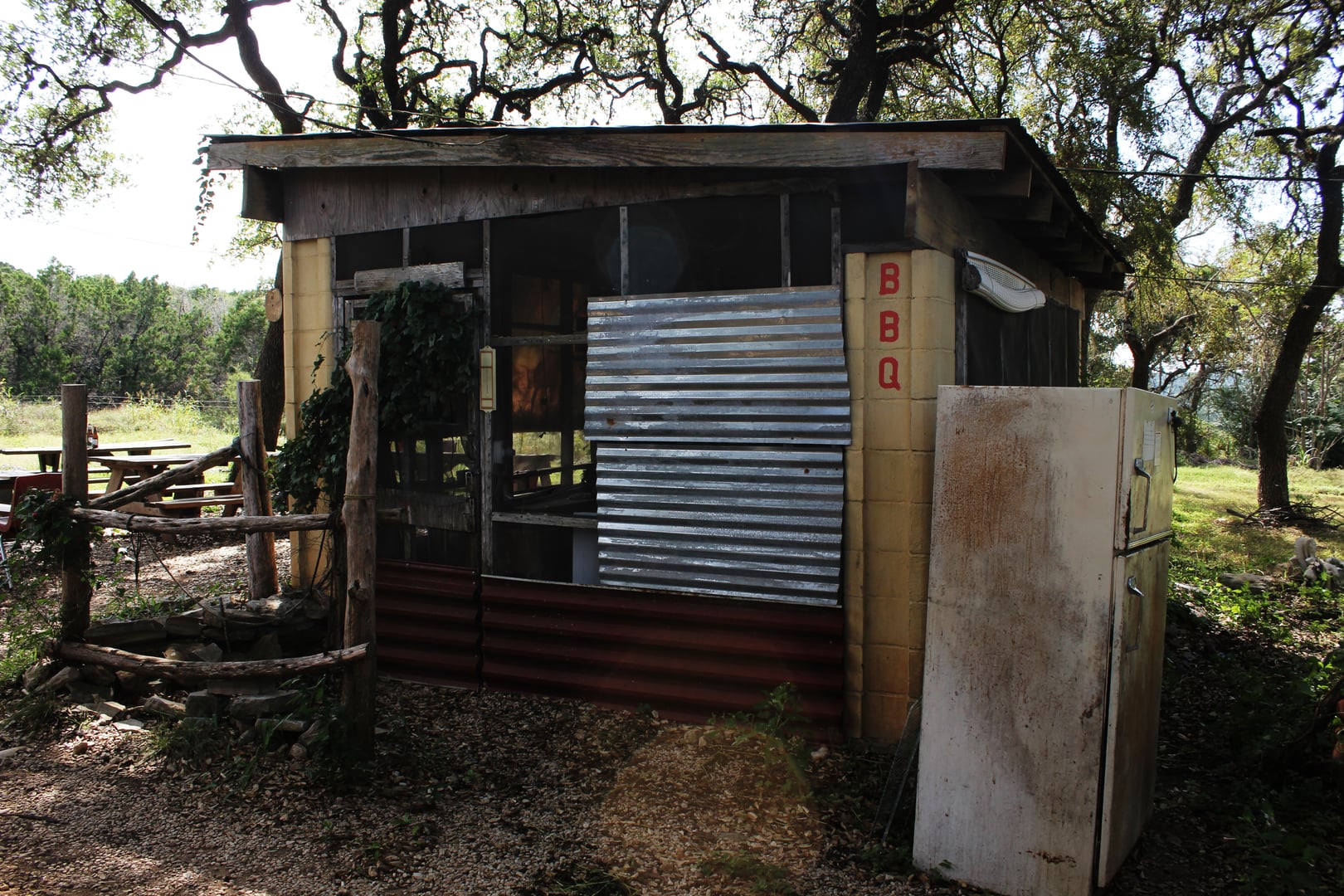 Rustic facade of Devil's Backbone Tavern along Ranch Road 32 in Fischer, Texas — a low stone-and-wood roadhouse with a gravel lot and Hill Country cedar trees