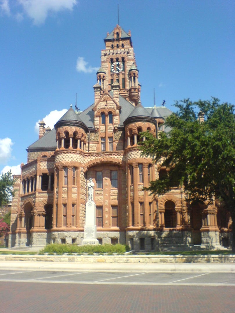 Exterior of the 1897 Ellis County Courthouse in Waxahachie Texas, a Richardsonian Romanesque building with stone carvings and a clock tower