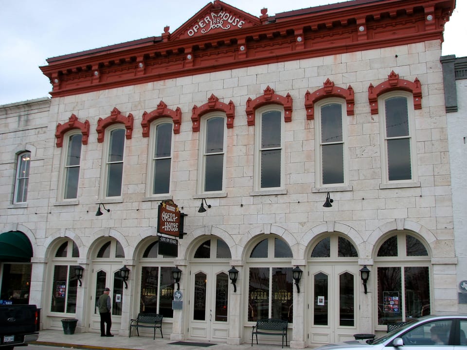 Close view of the Granbury Opera House on the town square in Granbury, Texas, with the pediment lettered 'Opera House 1886', red-trimmed arched upper windows, hanging theatre sign and arcaded ground floor, in 2009.
