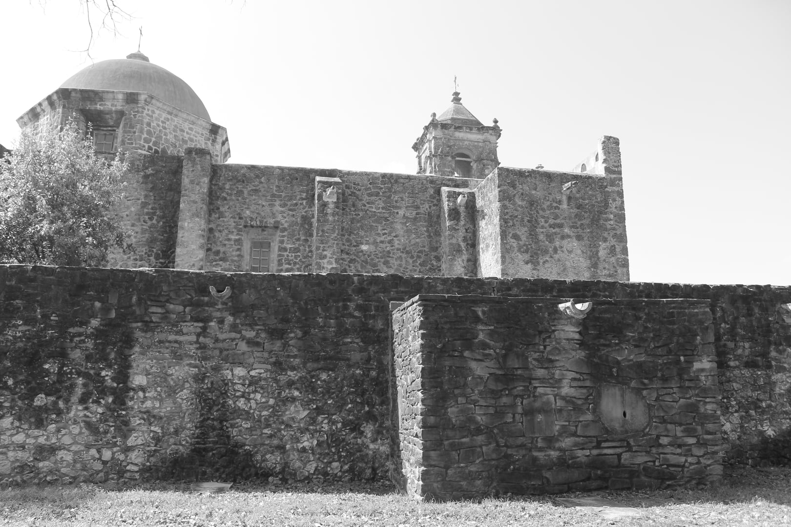Stone chapel facade of Mission San Francisco de la Espada in San Antonio, Texas, with wooden door and cross above the entrance