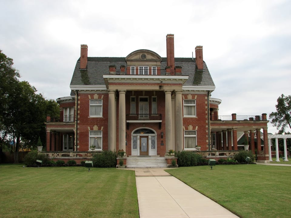 The front of Thistle Hill (the Wharton-Scott House) in Fort Worth, Texas, seen straight on from the entrance walk, with the two-storey columned portico, entrance steps, pedimented dormer and brick chimneys, in 2009.