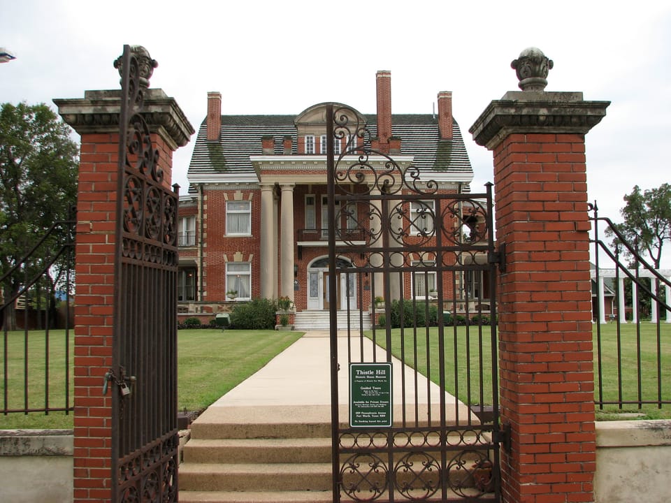 The brick gateposts and wrought-iron entrance gate of Thistle Hill (the Wharton-Scott House) in Fort Worth, Texas, with the house at the end of the walk beyond, in 2009.