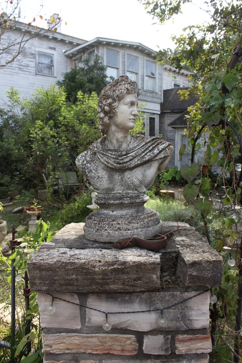 A classical garden bust on a stone pier on the grounds of Victoria's Black Swan Inn, with the house visible behind.