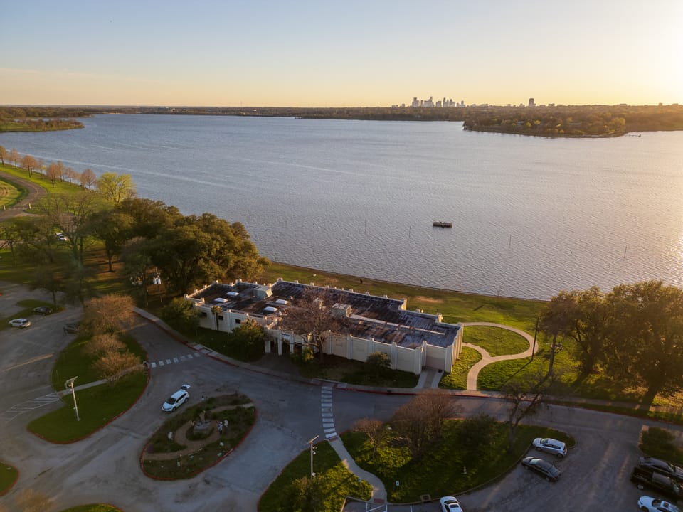 Aerial view of the Bath House Cultural Center on the shore of White Rock Lake, with the Dallas skyline on the horizon.