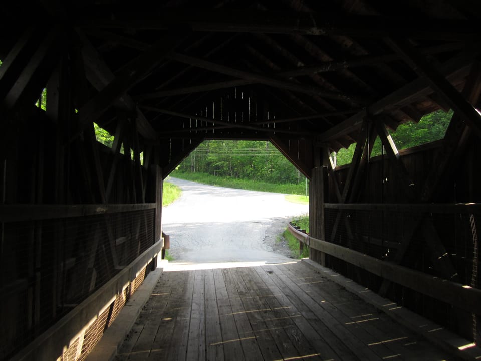 Inside the Gold Brook Covered Bridge (Emily's Bridge) in Stowe, Vermont, looking along the plank deck between the timber truss walls to the road beyond, July 2011.