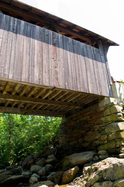 The side of the Gold Brook Covered Bridge (Emily's Bridge) in Stowe, Vermont, seen from below, showing the weathered board siding, the timber floor beams and the stone abutment, June 2011.