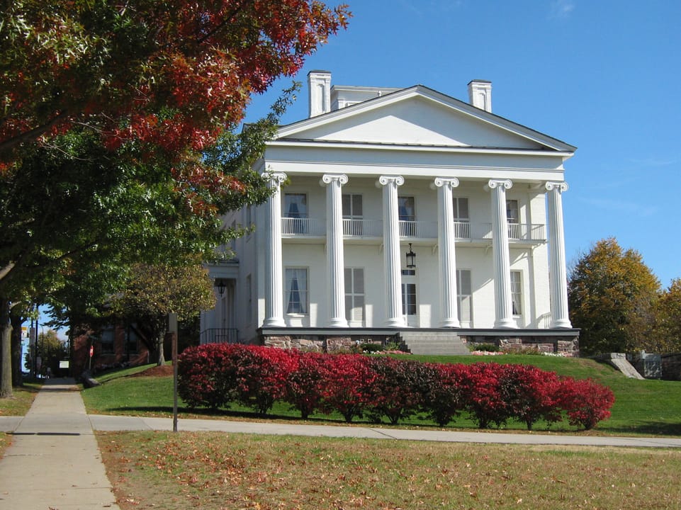 Follett House in autumn, with its front portico and red foliage along the walkway; the building is home to Pomerleau Real Estate.