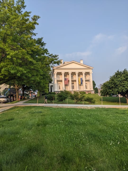A wide view of Follett House set back on its lawn, seen from College Street through the surrounding trees.