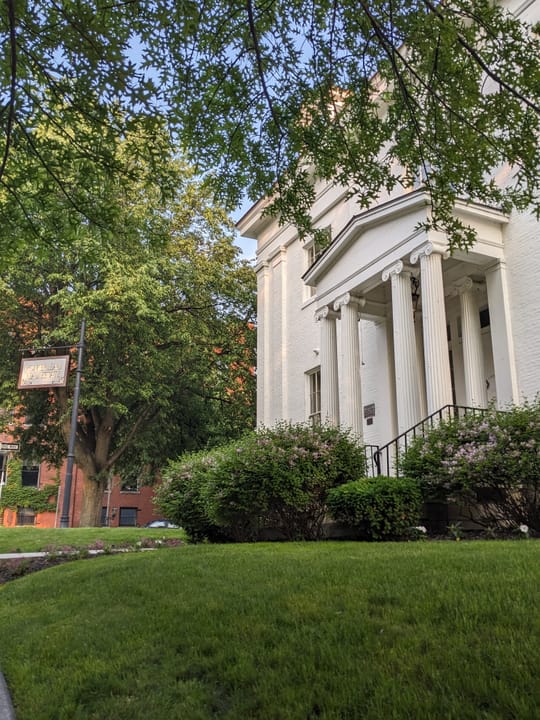 Follett House's portico seen from the front walkway, framed by the canopy of a street tree.