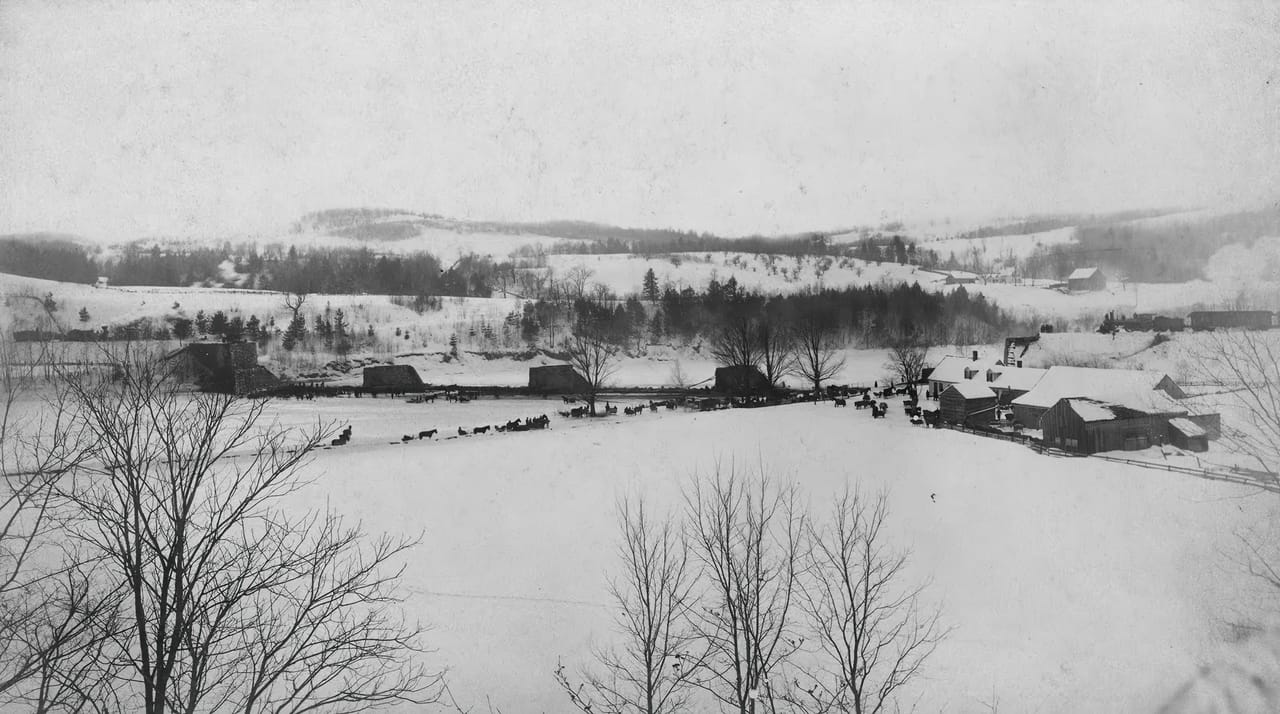 A wide winter view of the White River valley at West Hartford, Vermont, showing the ruined stone piers of the Central Vermont Railway bridge after the February 5, 1887 derailment and fire, with the Paine house at right. The river is frozen and crosse