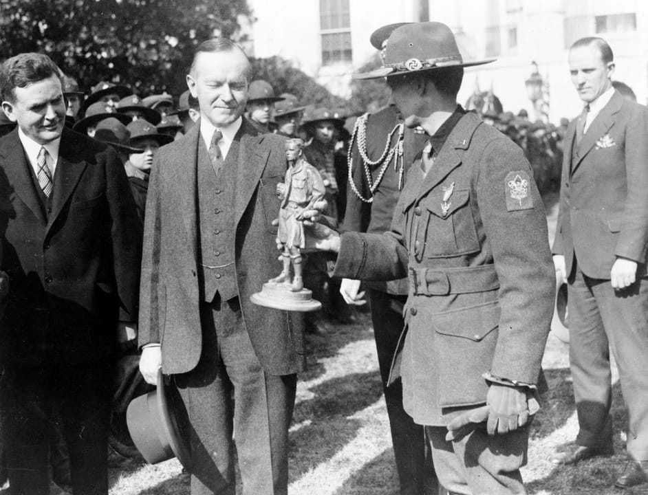 Title: President greets visiting boy scouts. 1500 boy scouts from N.Y., N.J., &amp; Conn. making annual pilgrimage to the Capitol being greeted at the White House by President Coolidge
President Calvin Coolidge receiving statue of Boy Scout, outside the White House
Abstract/medium: 1 photographic pr