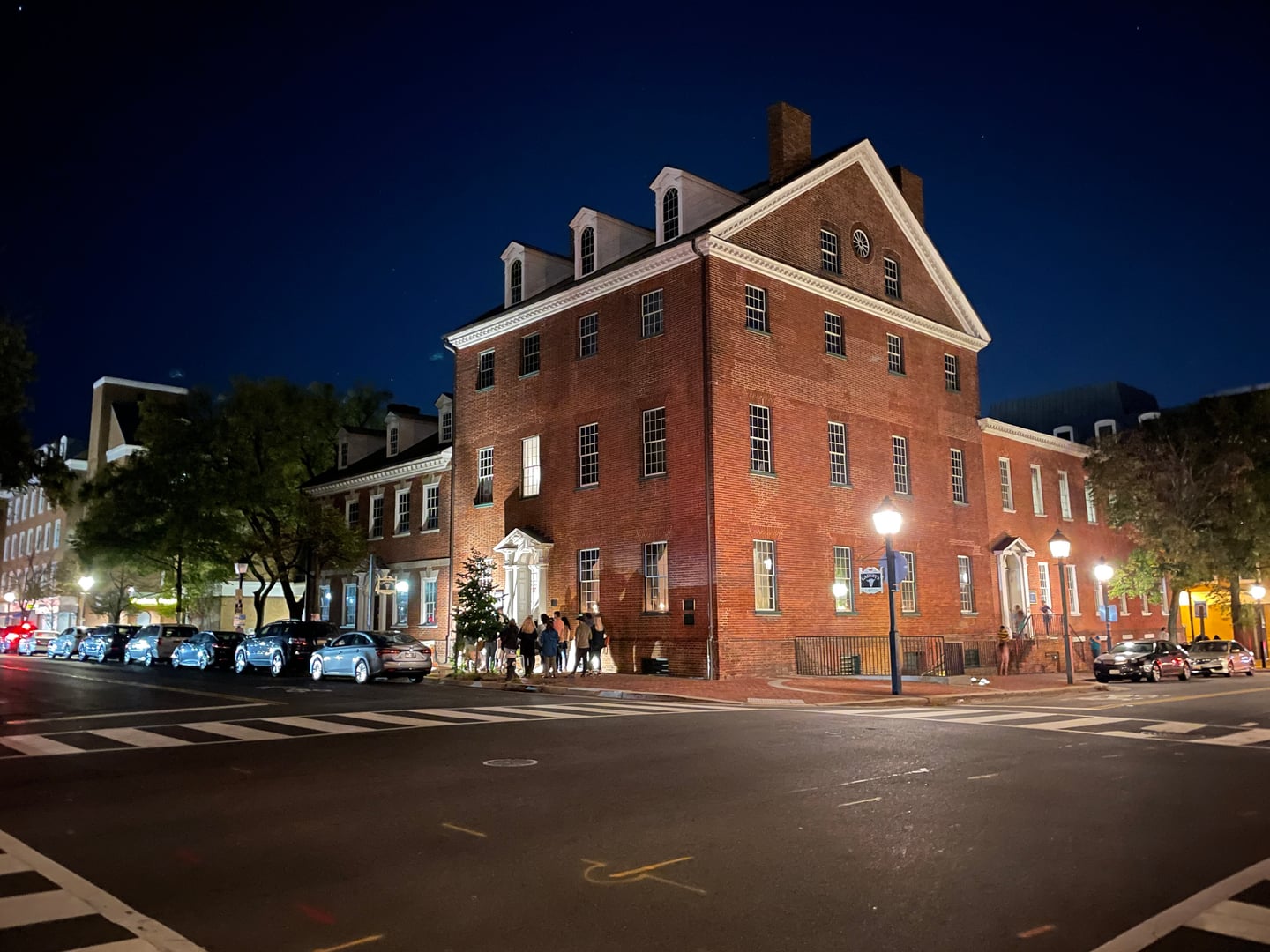 Gadsby's Tavern at night, at North Royal and Cameron Streets in Old Town Alexandria, with people gathered on the sidewalk; a stop on the tour's North Route.