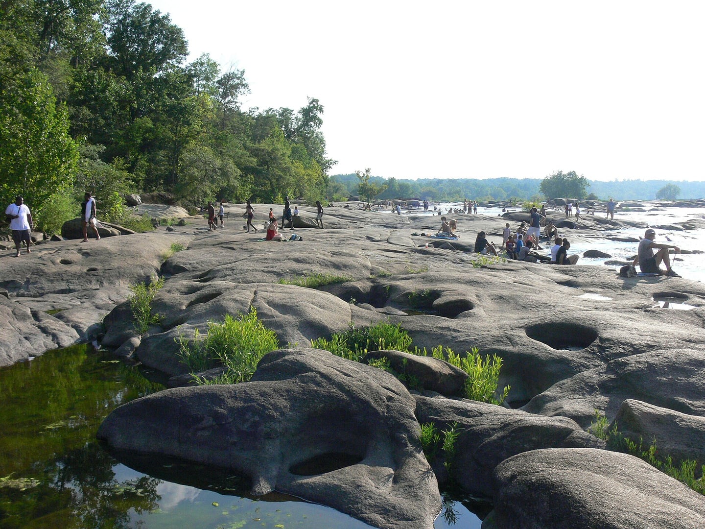 Visitors on the granite rocks along the James River shoreline of Belle Isle, Richmond, Virginia, with the city visible in the background