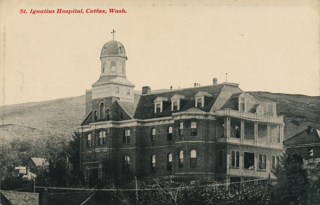 St. Ignatius Hospital, Colfax, Washington, circa 1915, in a postcard showing the domed tower and east wing from an elevated angle, with the Palouse hills behind