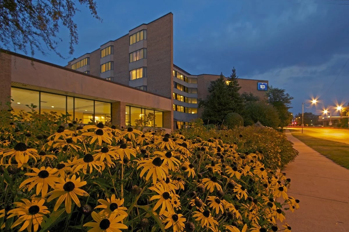 Hotel Mead resort and conference center exterior at dusk in Wisconsin Rapids, Wisconsin, with lit windows and yellow Black-eyed Susan flowers in front