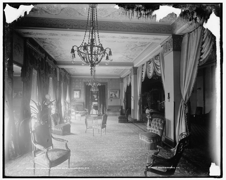 The Parlor at the Pfister Hotel, c.1900-1905 -- Victorian furnishings, drapery and a crystal chandelier in one of the hotel's public rooms, consistent with its renowned Victorian-art collection.