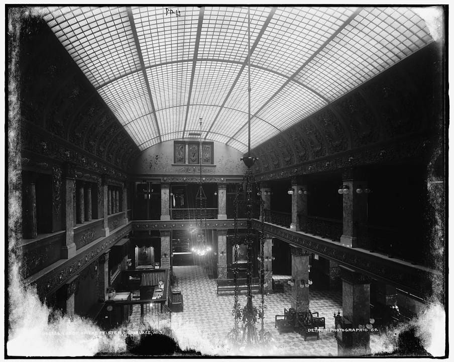 The lobby/arcade of the Pfister Hotel, c.1900-1905, looking down the two-story atrium under its glass barrel-vault skylight.