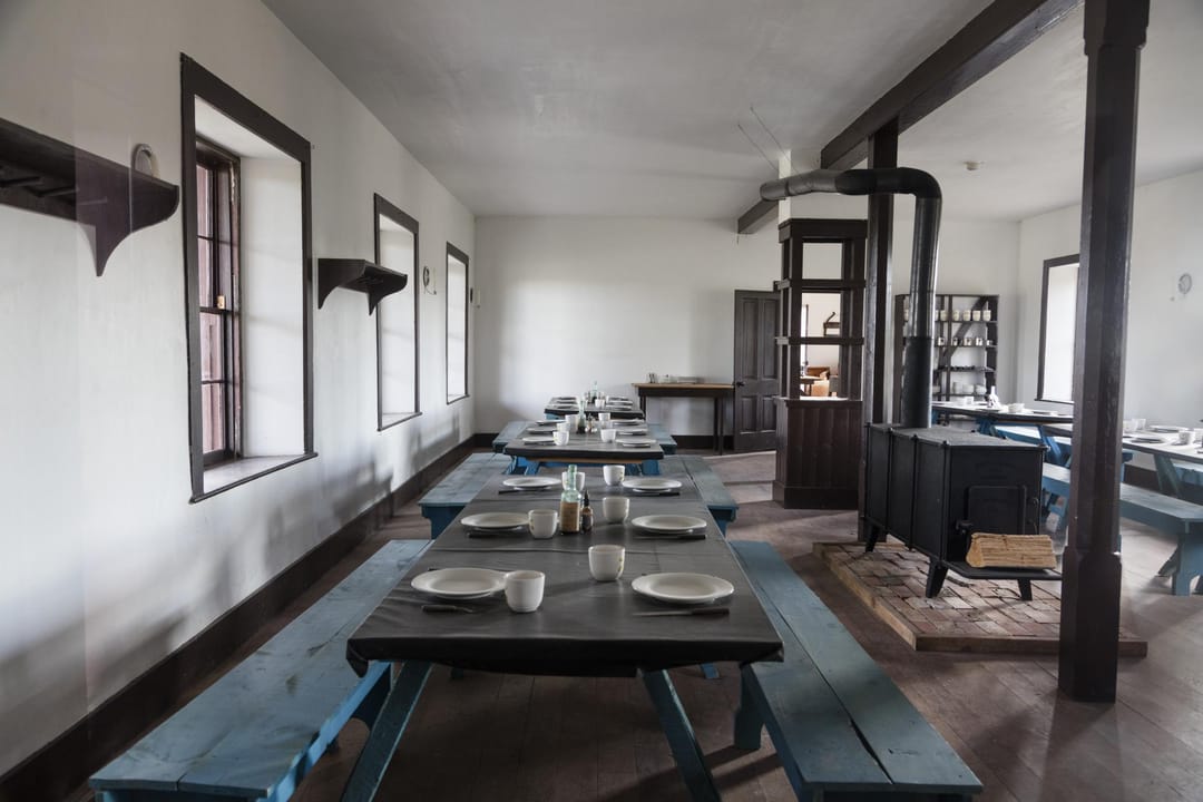 The restored enlisted men's dining quarters at Fort Laramie -- long mess tables and benches set for a meal, a public NPS-restored interior.