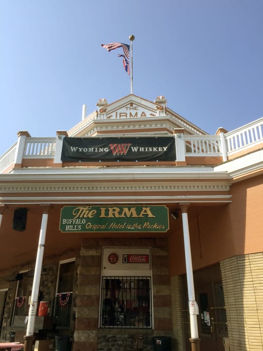 Full front view of Buffalo Bill's Irma Hotel, Cody, Wyoming, with flags flying from its balustraded porch.