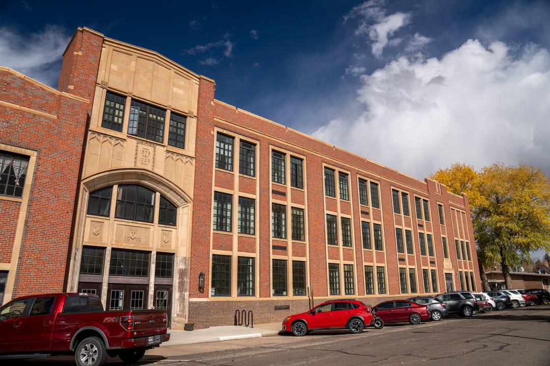 The stone-trimmed entrance bay with its datestone and the long three-storey brick wing of the Laramie Plains Civic Center, the former East Side School, Laramie, Wyoming, October 2025.