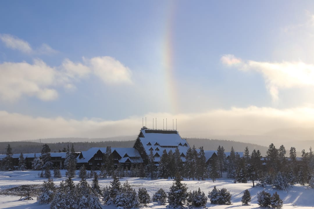 A sundog (rainbow-like ice-crystal halo) over the snow-covered Old Faithful Inn, Yellowstone National Park, winter 2022.